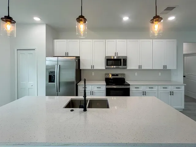 a kitchen with stainless steel appliances granite countertop a sink a stove a refrigerator and white cabinets with wooden floor