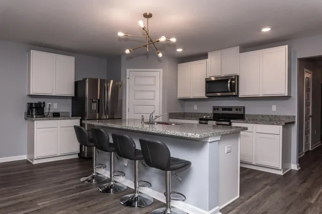 a kitchen with stainless steel appliances granite countertop a sink a stove a refrigerator cabinets and a dining table with wooden floor