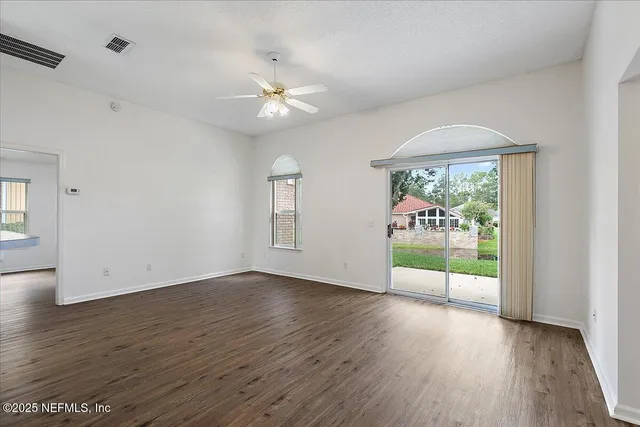an empty room with wooden floor fan and windows