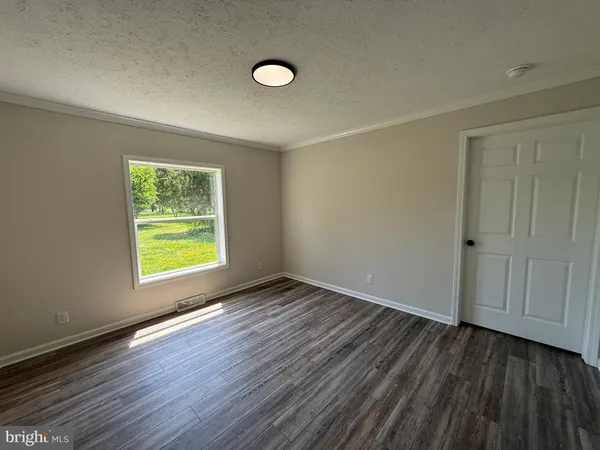 an empty room with wooden floor kitchen appliances and windows