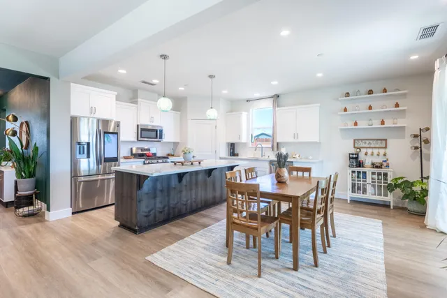 a room with stainless steel appliances kitchen island granite countertop wooden floor dining table and chairs