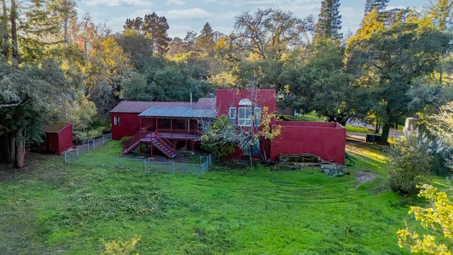 a view of a barn in front of a yard with large trees
