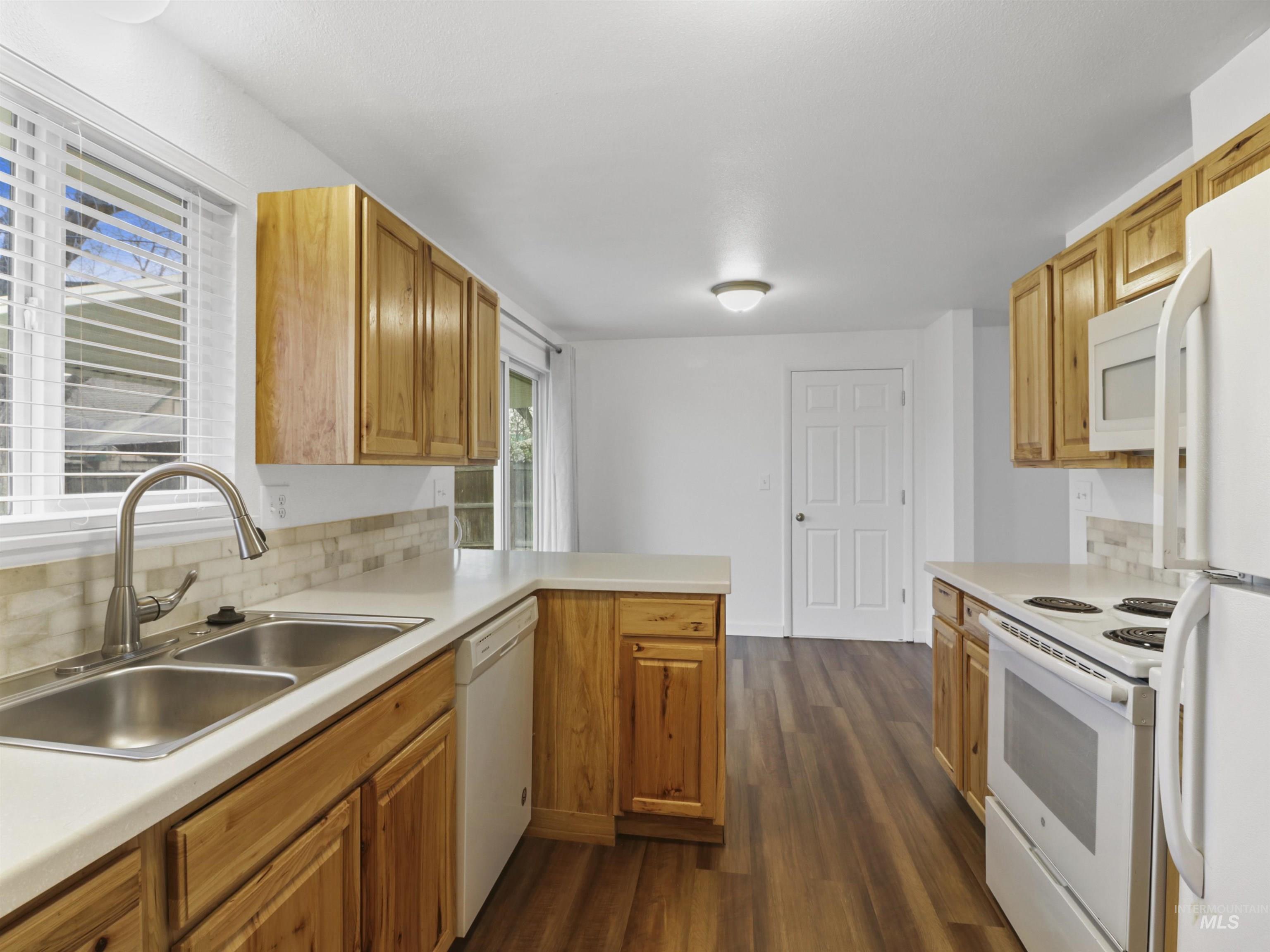 6739 West Grunder Street Boise, ID 83709 - Photo 11 of 24 Kitchen with backsplash, light countertops, white appliances, and dark wood-style flooring