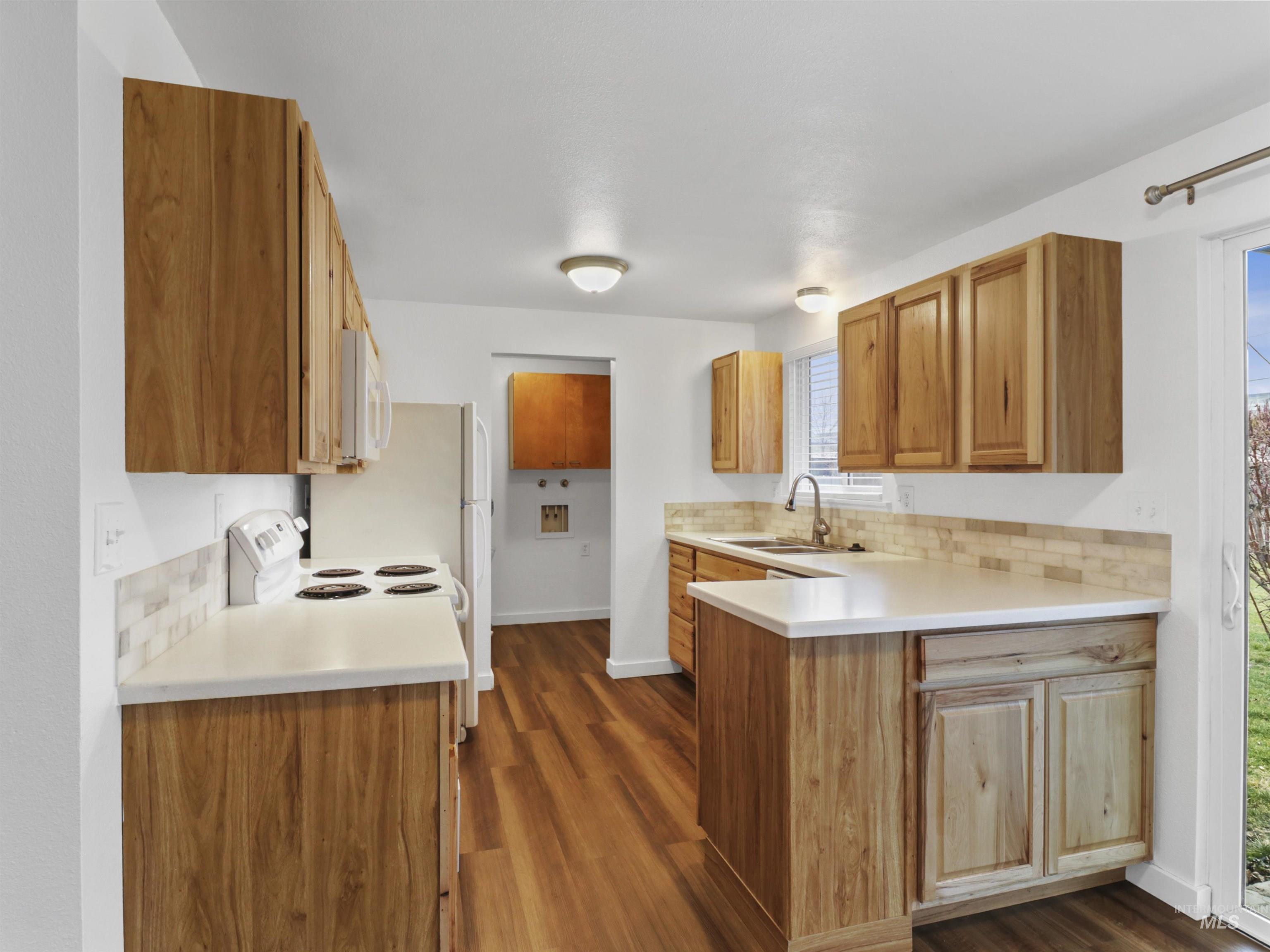 6739 West Grunder Street Boise, ID 83709 - Photo 9 of 24 Kitchen featuring tasteful backsplash, dark wood finished floors, a peninsula, white microwave, and brown cabinetry