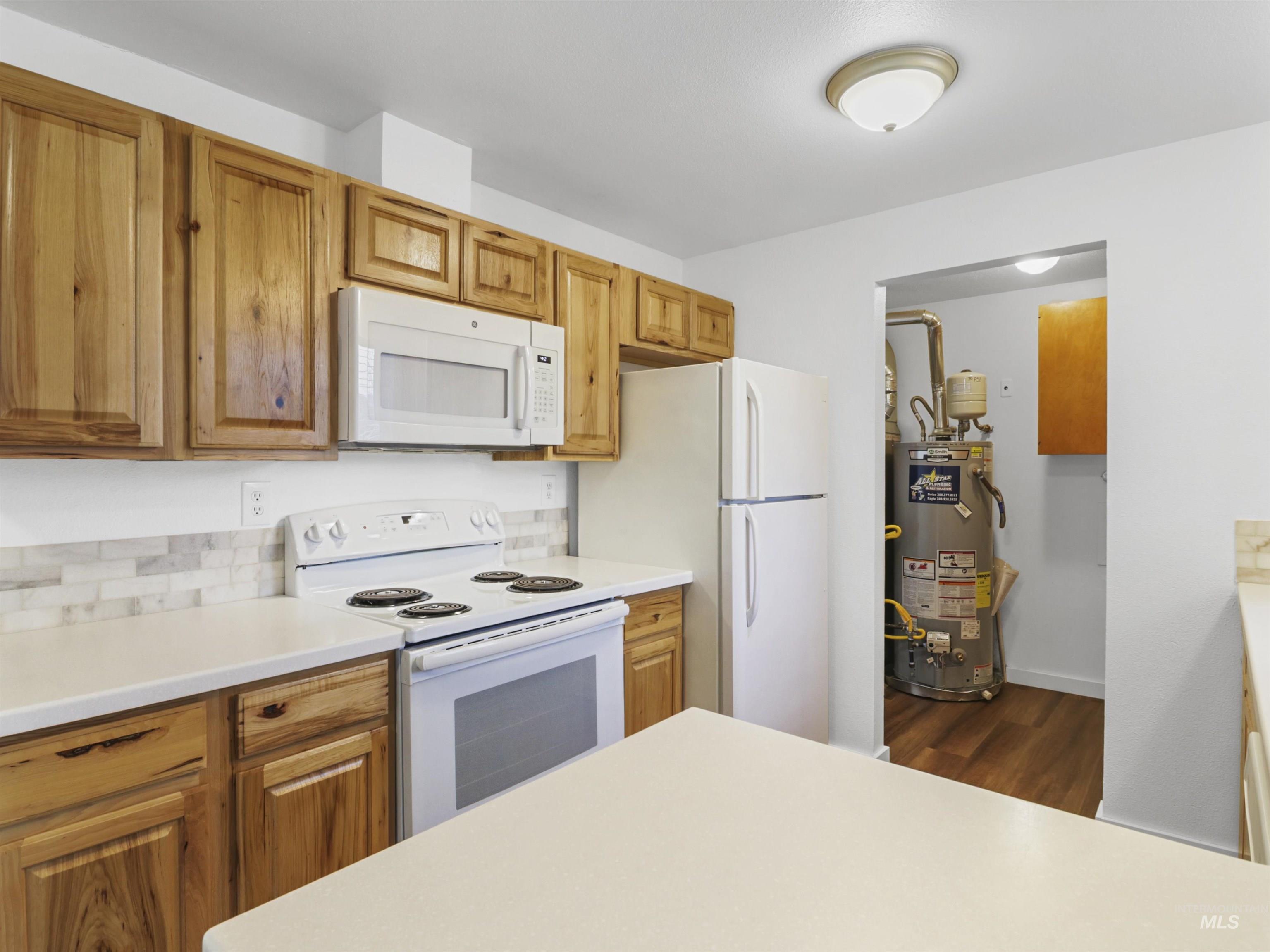 6739 West Grunder Street Boise, ID 83709 - Photo 10 of 24 Kitchen featuring white appliances, light countertops, water heater, dark wood-style flooring, and brown cabinets