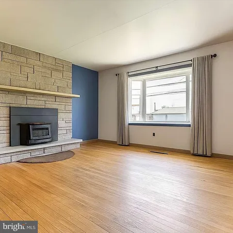 a view of an empty room with wooden floor fireplace and a window