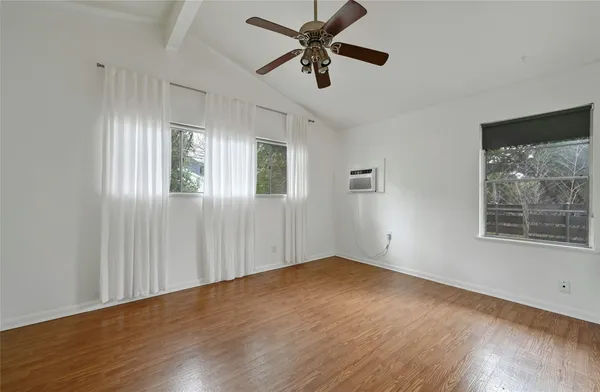 an empty room with wooden floor fan and windows