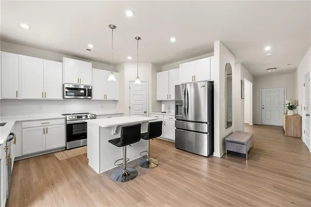 a kitchen with stainless steel appliances granite countertop a refrigerator a stove a sink dishwasher a dining table and chairs with wooden floor