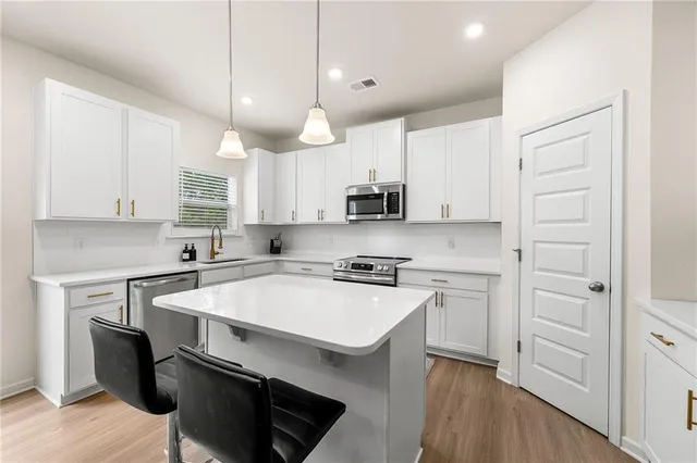 a kitchen with stainless steel appliances a sink a stove a refrigerator cabinets and chairs