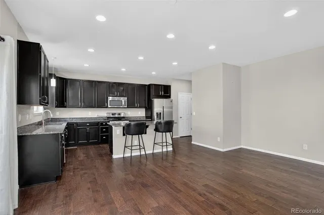 a kitchen with stainless steel appliances kitchen island granite countertop a stove top oven a sink a dining table and chairs with wooden floor