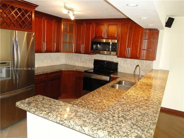 a kitchen with kitchen island granite countertop wooden cabinets a refrigerator and a sink