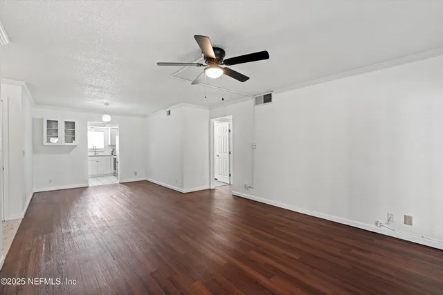 a view of an empty room with wooden floor and a ceiling fan