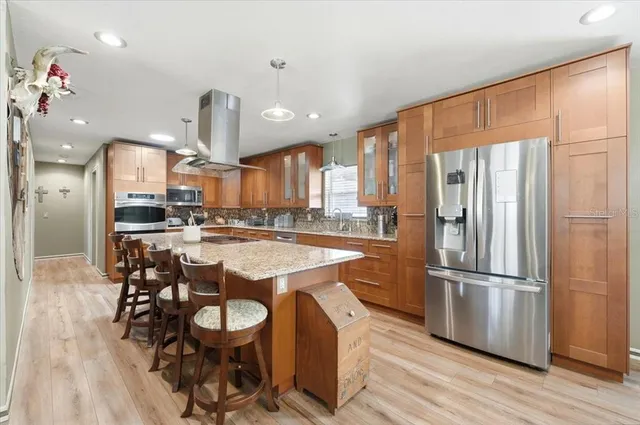 a large kitchen with stainless steel appliances kitchen island granite countertop a table chairs and a refrigerator