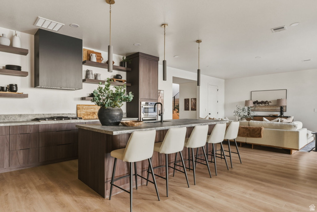 923 North Emery Lane Elk Ridge, UT 84651 - Photo 54 of 101 Open-concept kitchen featuring dark wood-finish cabinetry, stone countertops, a large center island with pendant lighting, and light wood-finish flooring