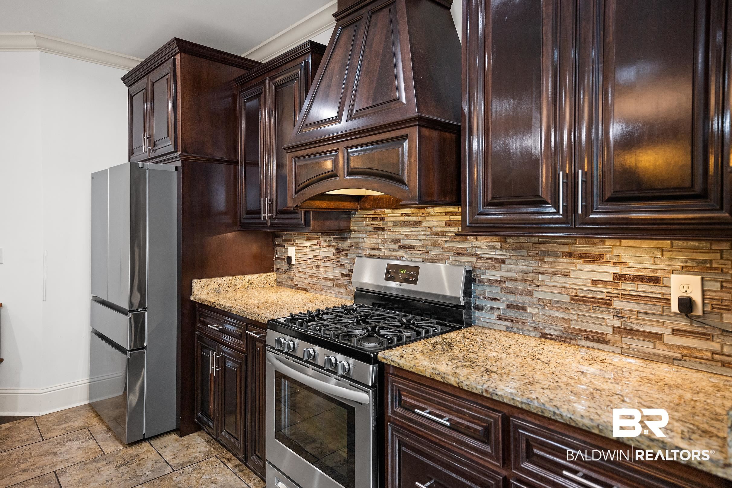 313 Pecan Ridge Boulevard Fairhope, AL 36532 - Photo 48 of 51 Kitchen featuring dark wood cabinetry, stainless steel appliances, a multi-tone tile backsplash, light-colored countertops, and tiled flooring