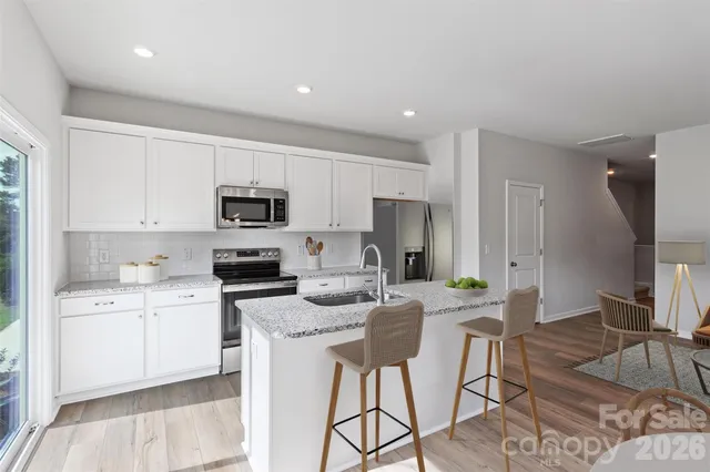 a kitchen with stainless steel appliances granite countertop a stove top oven a sink a refrigerator and white cabinets with wooden floor