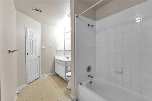 a bathroom with a tub shower sink vanity and toilet