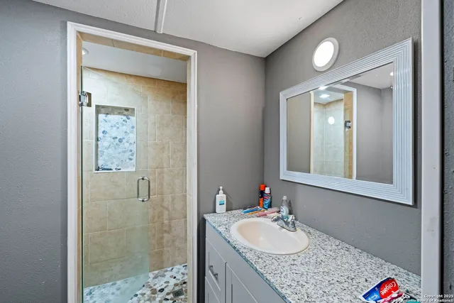 a bathroom with a granite countertop sink a mirror and shower