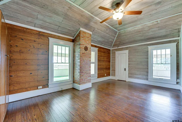 an empty room with wooden floor chandelier fan and windows