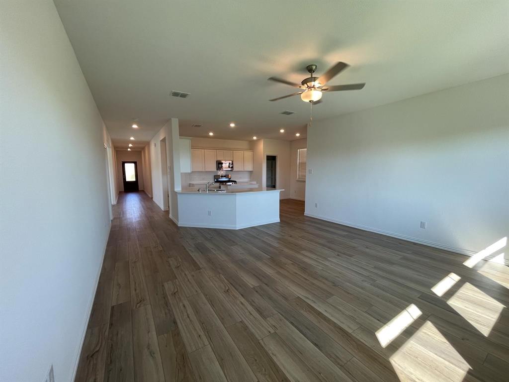 3305 Tulip Poplar Trail McKinney, TX 75071 - Photo 19 of 29 a view of a livingroom with a kitchen island wooden floor and a ceiling fan