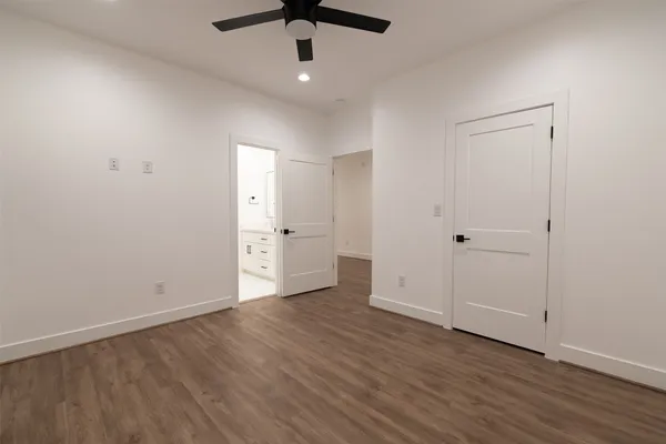 an empty room with wooden floor a ceiling fan and kitchen view