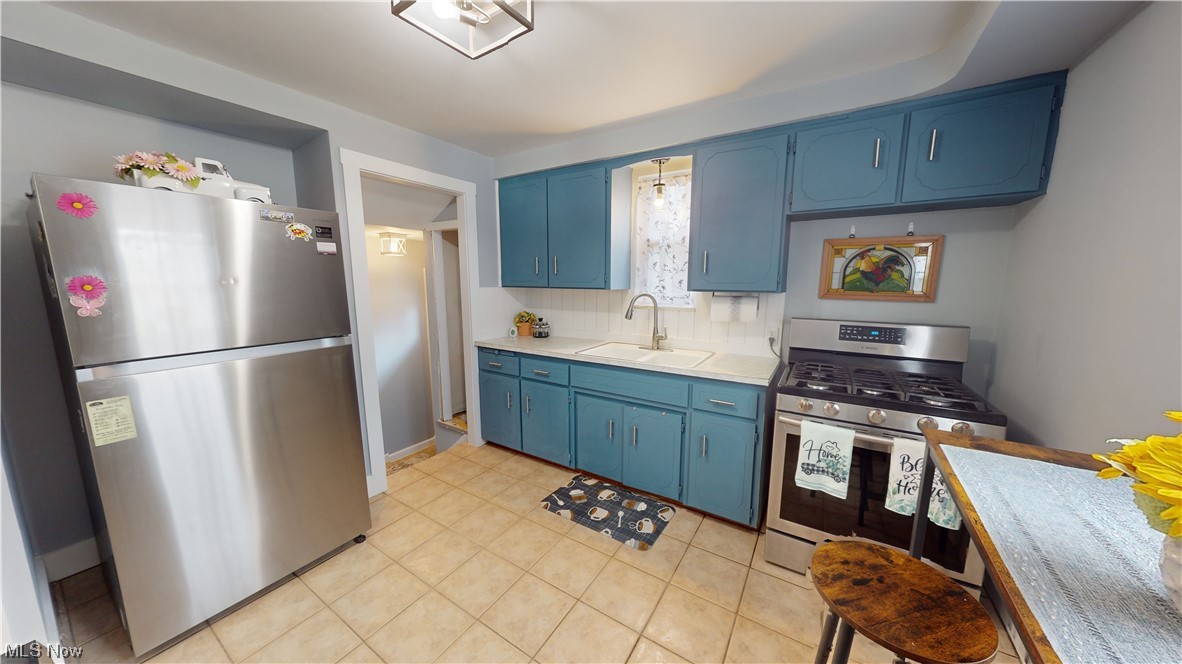 1331 Churchill Road Lyndhurst, OH 44124 - Photo 18 of 35 Kitchen featuring blue cabinets, sink, tasteful backsplash, stainless steel appliances, and light tile floors