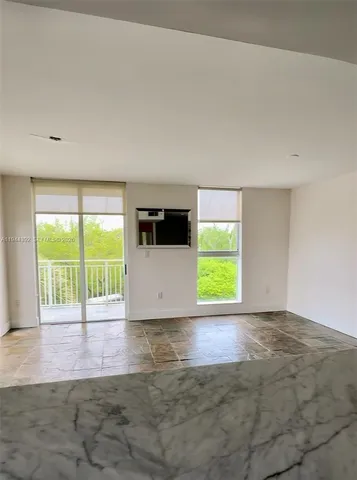 a view of an empty room with a window and a kitchen view