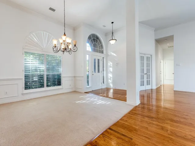 a view of an empty room with wooden floor and a chandelier