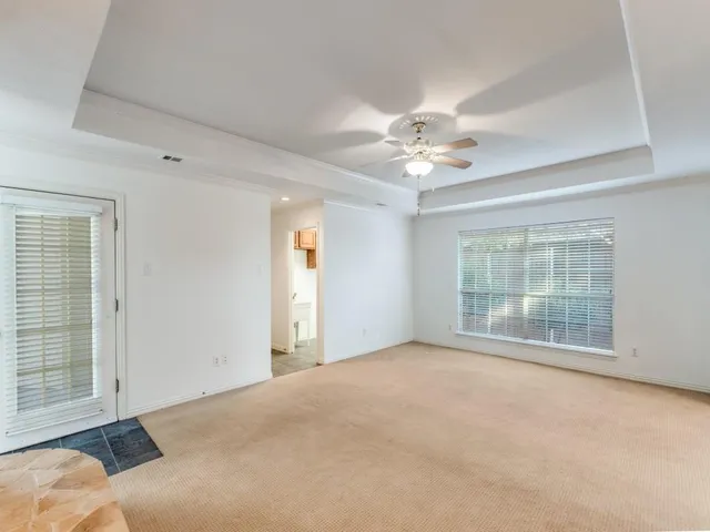 an empty room with chandelier fan and windows
