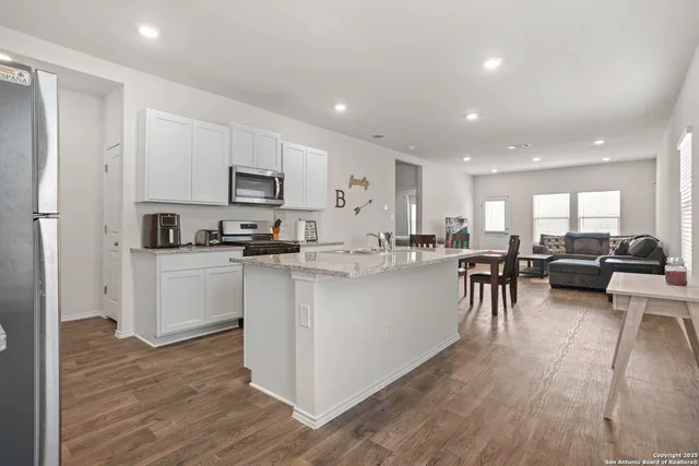 a kitchen with stainless steel appliances granite countertop a refrigerator a stove top oven a sink and white cabinets with wooden floor