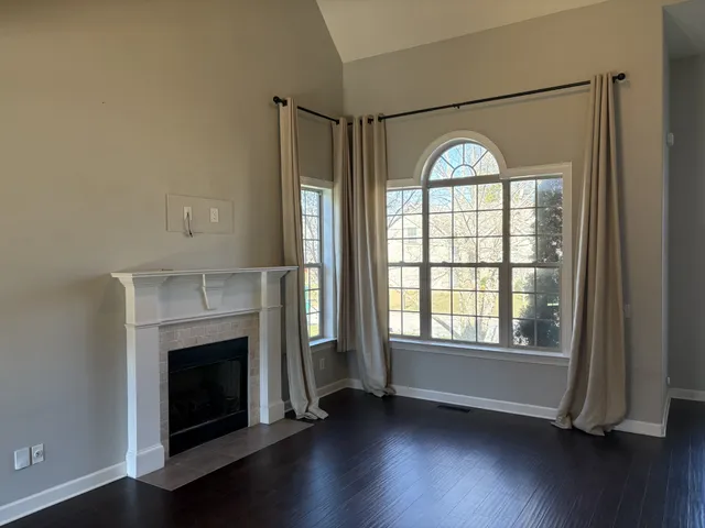 an empty room with wooden floor fireplace and windows