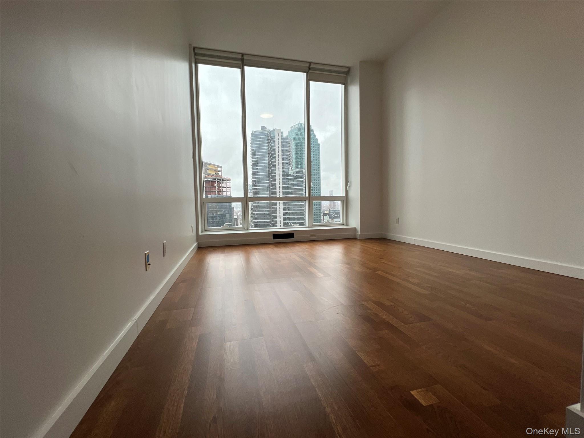27-17 42nd Road, Unit 23C Queens, NY 11101 - Photo 6 of 14 Empty room with dark wood-type flooring and a city view