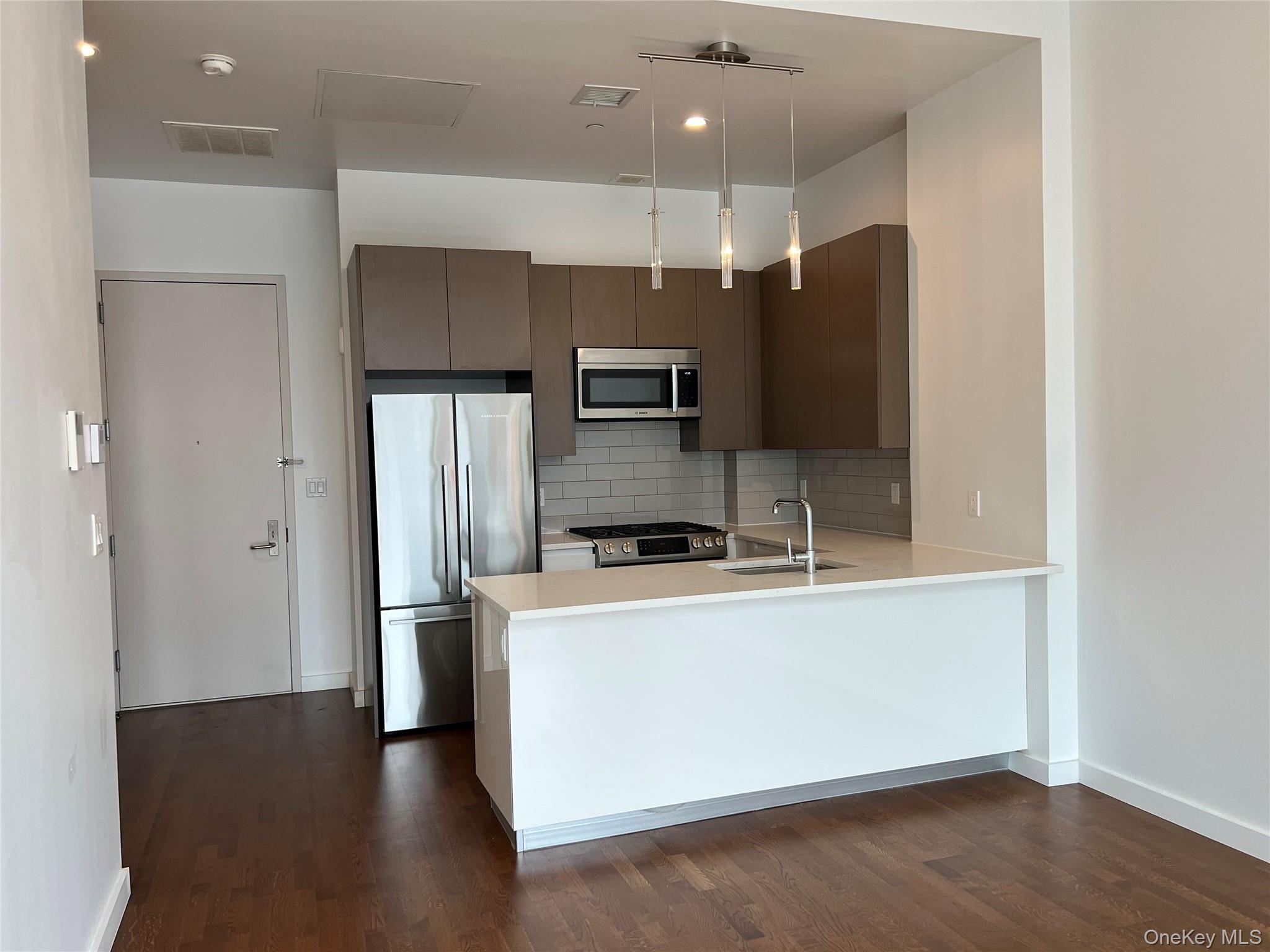 27-17 42nd Road, Unit 23C Queens, NY 11101 - Photo 7 of 14 Kitchen with stainless steel appliances, backsplash, hanging light fixtures, a peninsula, and dark wood-style flooring