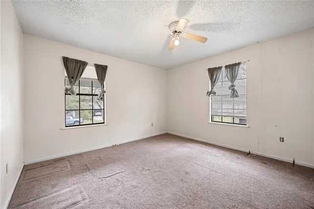 an empty room with windows and chandelier fan