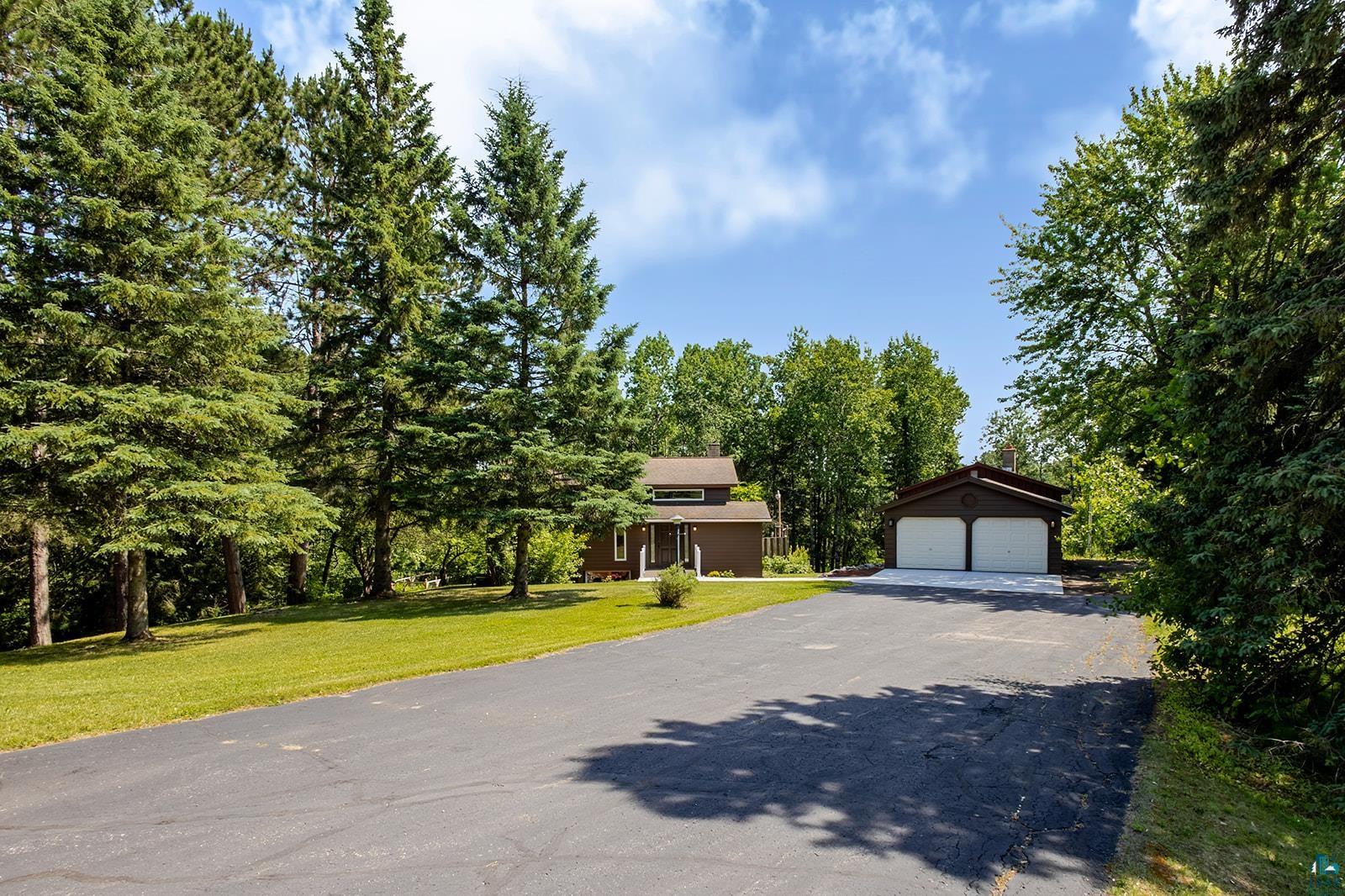 29 Ridge Road Esko, MN 55733 - Photo 3 of 41 Asphalt driveway leading to a detached two-car garage with white doors, surrounded by mature trees