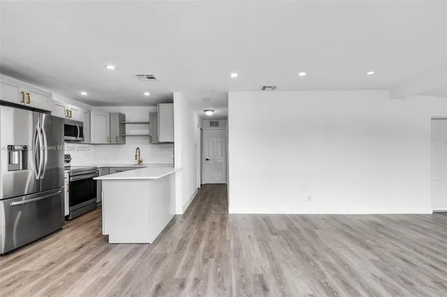 a large kitchen with a center island wooden floor stainless steel appliances and cabinets