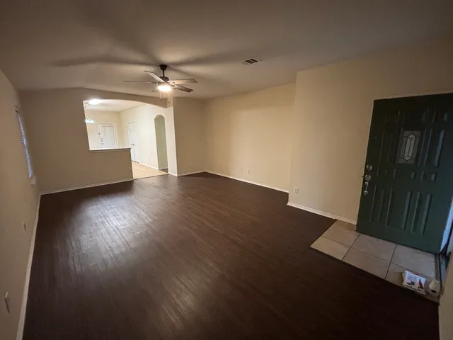 a view of an empty room with wooden floor and a ceiling fan