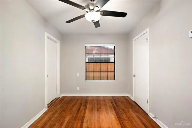an empty room with wooden floor chandelier fan and windows