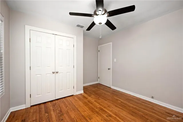 an empty room with wooden floor fan and windows