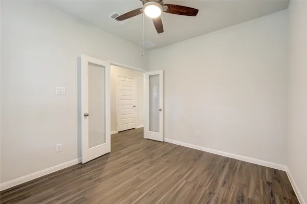 an empty room with wooden floor chandelier fan and windows