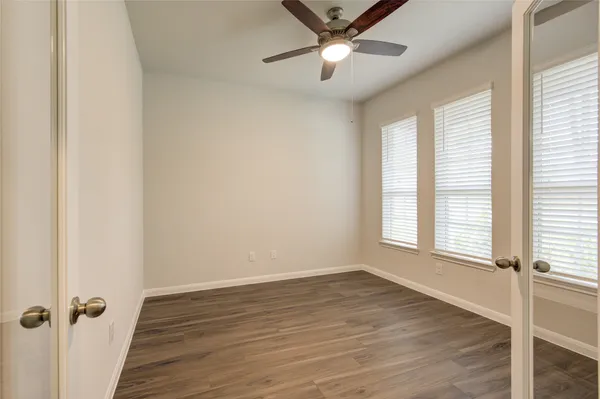 an empty room with wooden floor fan and windows
