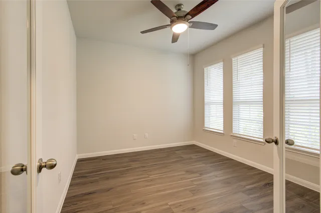 an empty room with wooden floor fan and windows