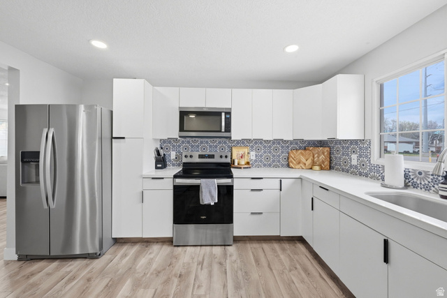 1795 South 200 West Bountiful, UT 84010 - Photo 10 of 37 Kitchen with stainless steel appliances, white cabinetry, light wood-type flooring, recessed lighting, and backsplash