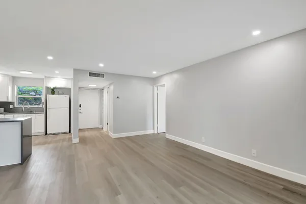 a view of an empty room with wooden floor and a kitchen
