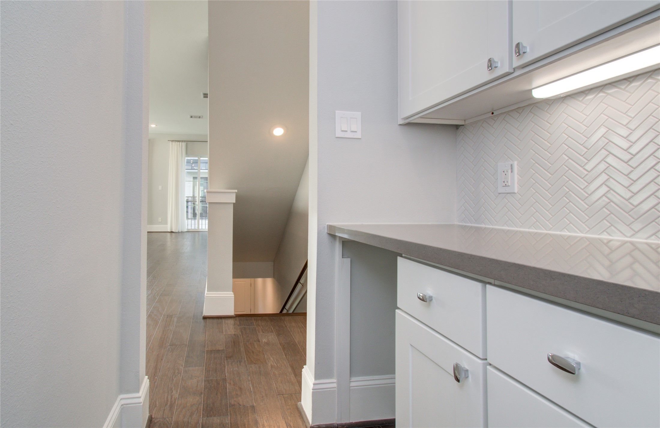 1262 North Post Oak Road, Unit A Houston, TX 77055 - Photo 17 of 50 A built-in butler's pantry or wet bar area highlights dark stone countertops paired with white shaker cabinetry and a herringbone tile backsplash. Under-cabinet lighting illuminates the workspace adjacent to the main hallway.