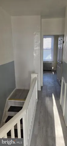 a view of a hallway to a livingroom with wooden floor and staircase