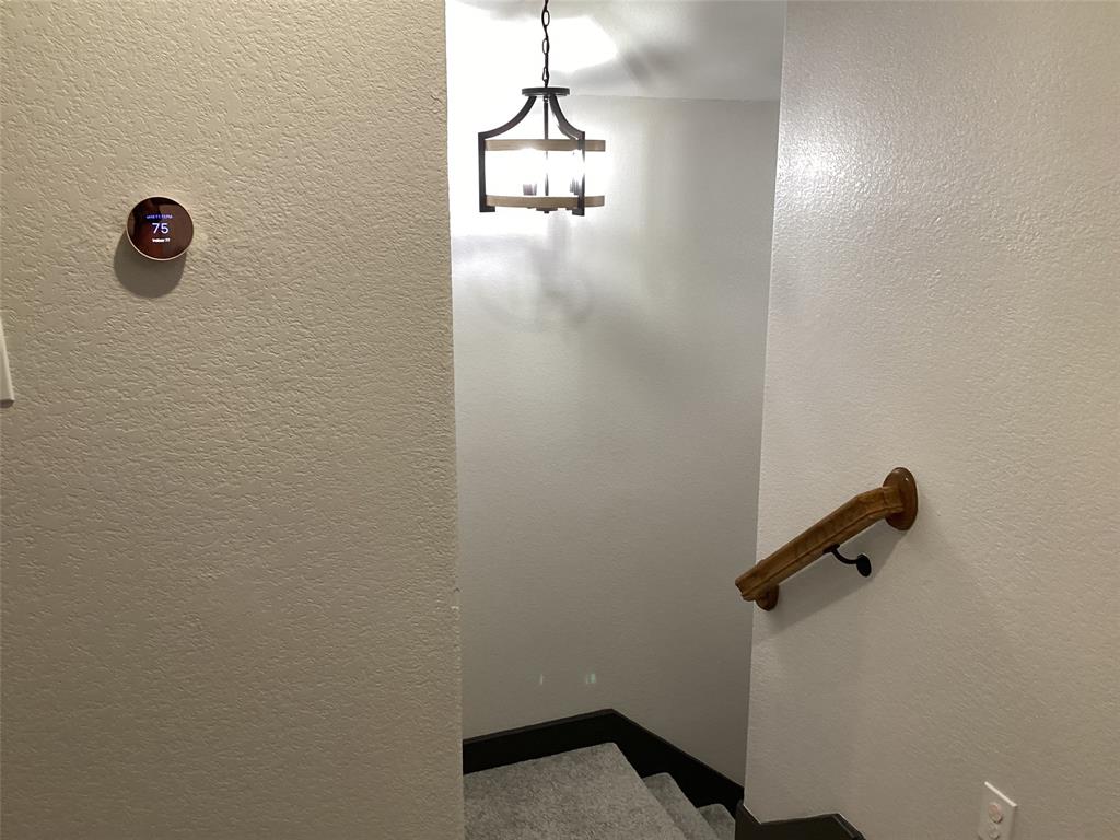 10320 Point Lobos Trail Fort Worth, TX 76177 - Photo 23 of 33 Smart thermostat on a textured wall, with a wood and metal pendant light fixture illuminating a carpeted stairway featuring a wooden handrail