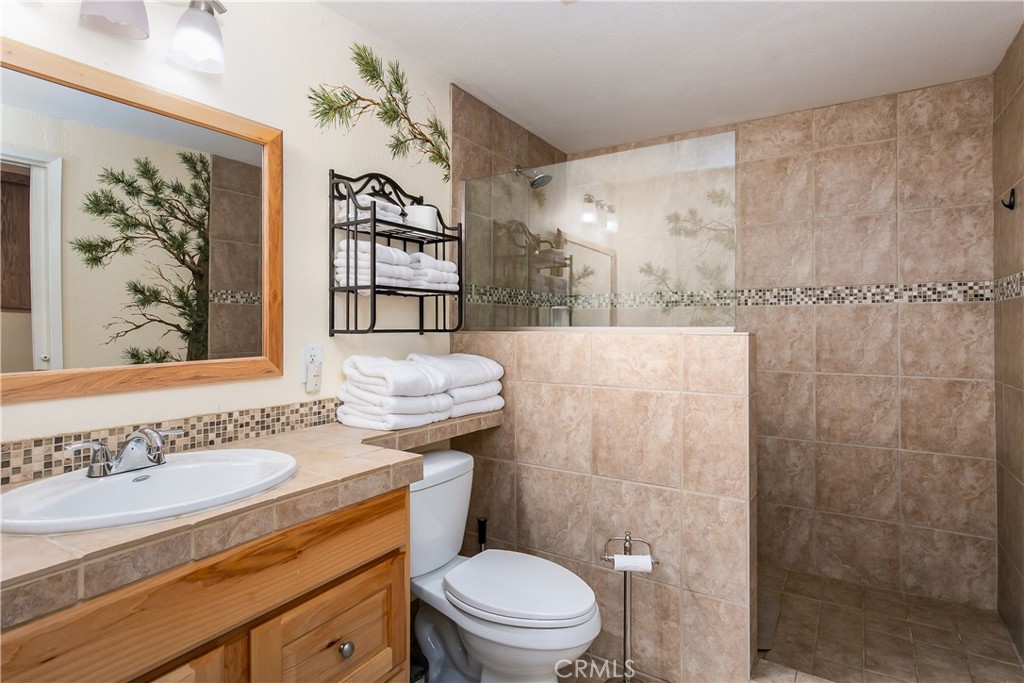 10960 Steinhoff Road Frazier Park, CA 93225 - Photo 43 of 46 The private en-suite bathroom located inside the downstairs 5th bedroom. This functional space features a warm oak vanity with a matching neutral countertop, a large framed wall mirror, and a spacious walk-in shower lined with large-format floor-to-ceiling tile and a decorative mosaic border.