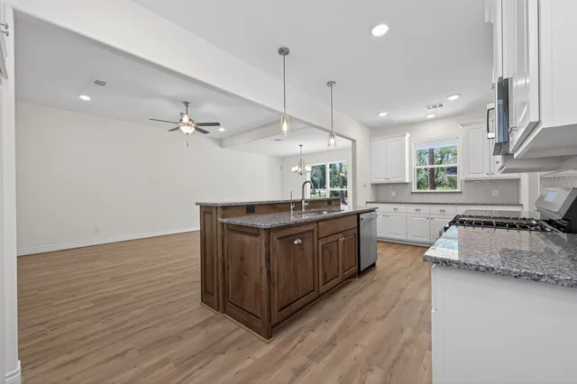 a kitchen with stainless steel appliances granite countertop a sink a stove a refrigerator cabinets and wooden floor