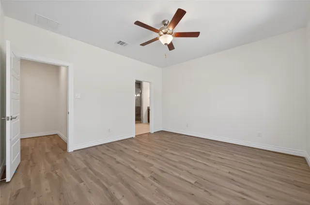 an empty room with wooden floor ceiling fan and windows